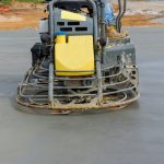 Concrete polishing machines are being used by workers to polish the cement after it has been poured on the foundation floor