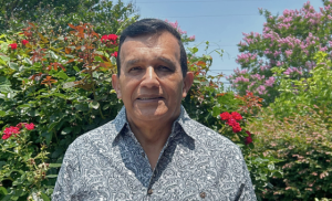 A picture of Luis from the shoulders up, standing in front of flowering plants